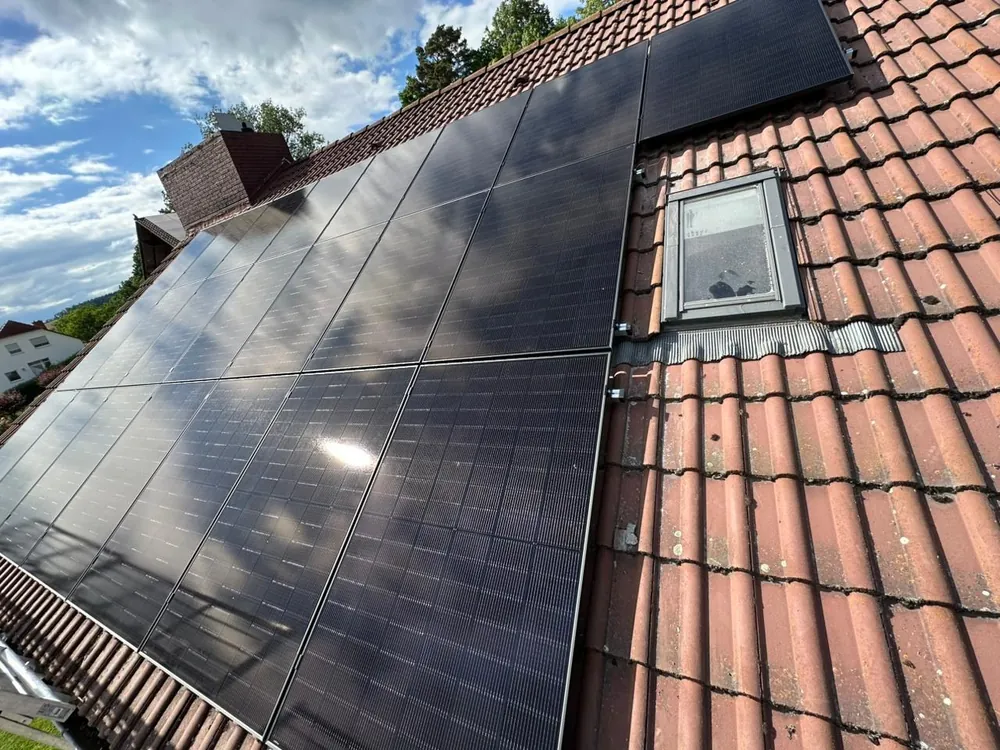 Ziegeldach mit Dachfenster und Modulen bis zum First, dramatischer Wolkenhimmel